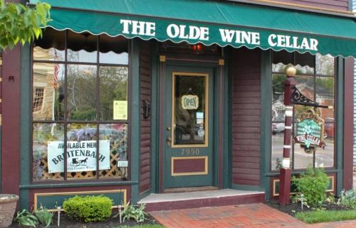 A quaint storefront of "The Olde Wine Cellar" with a welcoming open sign and decorative windows.