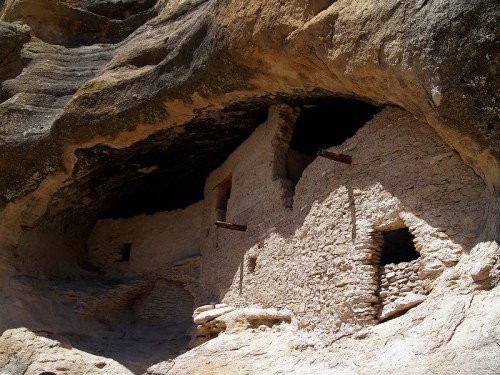 Ancient stone dwellings built into a rocky cliff, showcasing weathered walls and small windows.