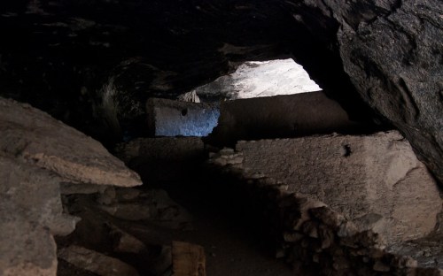 A dimly lit cave interior with stone walls and a bright opening in the distance, suggesting an exit.