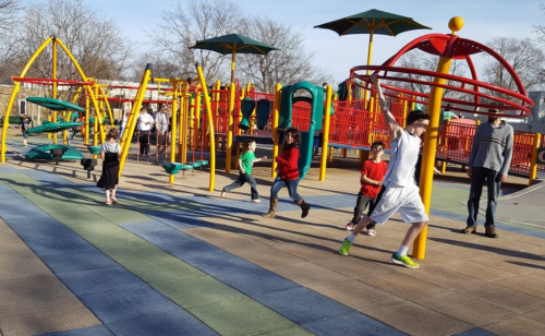 Children playing on a colorful playground with climbing structures and spinning equipment on a sunny day.