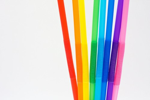 Colorful drinking straws in a gradient of red, orange, yellow, green, blue, and purple against a white background.