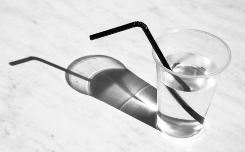 A clear cup of water with a black straw, casting a shadow on a light surface.