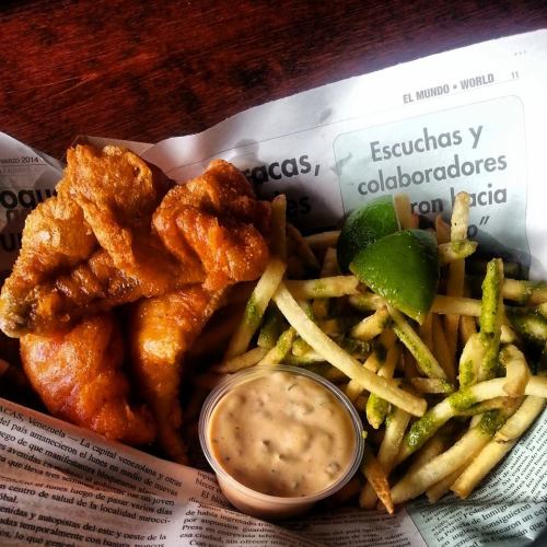 A plate of crispy fried chicken wings with seasoned fries and a dipping sauce, served on a newspaper.
