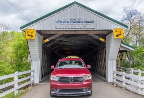 A red car drives through a covered bridge with a sign reading "Our Old Covered Bridge" in Newton Falls, Ohio.