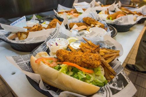 A spread of fried fish sandwiches and fries served in baskets lined with newspaper.