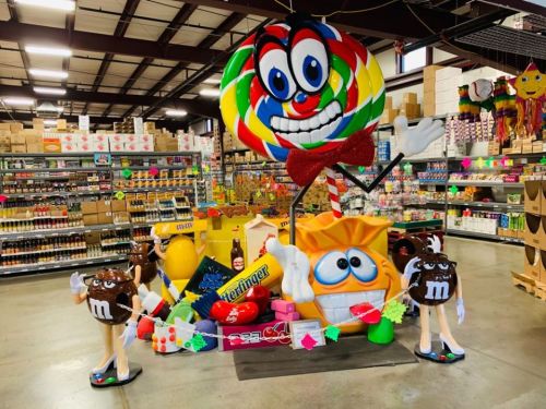 Colorful candy display featuring oversized lollipops, candy characters, and various sweets in a store setting.