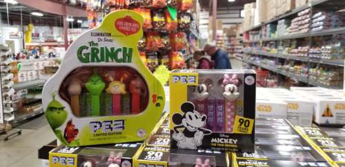 Two PEZ dispensers featuring The Grinch and Mickey Mouse, displayed in a store aisle filled with products.
