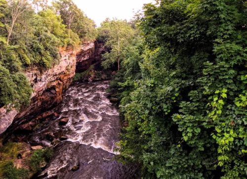 A winding river flows through a lush, green landscape with rocky cliffs and dense trees on either side.