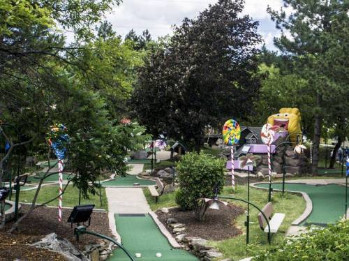 A colorful mini-golf course with candy-themed decorations and lush greenery under a cloudy sky.