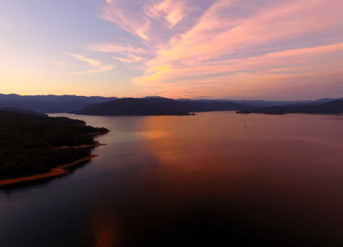 A serene lake at sunset, with vibrant colors reflecting on the water and mountains in the background.