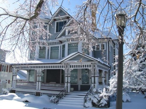 A large, Victorian-style house covered in snow, with intricate architectural details and a snowy landscape.