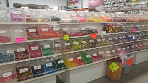 A colorful display of various candies in clear bins, organized on shelves with price tags visible.