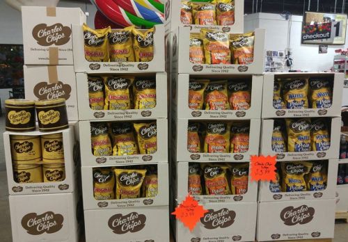 A display of stacked boxes and cans of Charles Chips snacks in a store, showcasing various flavors and prices.