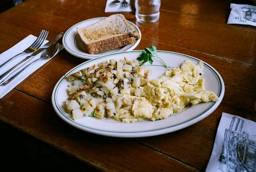 A plate of scrambled eggs, hash browns, and a slice of whole grain toast on a wooden table.