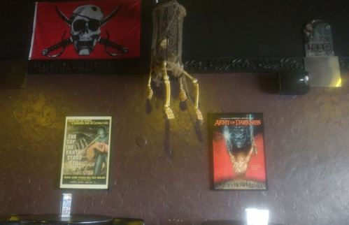 A dimly lit room featuring a pirate flag, a dreamcatcher, and vintage movie posters on the walls.