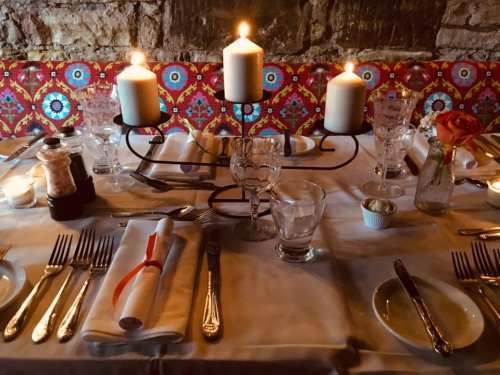 A beautifully set dining table with candles, glassware, and silverware, against a colorful patterned backdrop.
