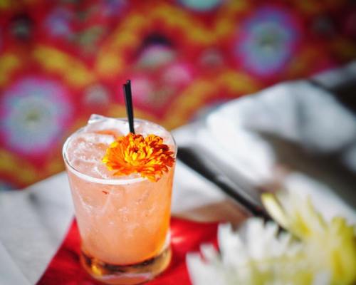 A refreshing cocktail garnished with a bright orange flower, set against a colorful, patterned background.