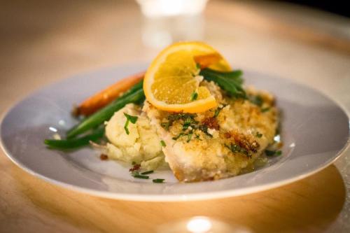 A plate of baked fish topped with orange slices, served with mashed potatoes and green beans.