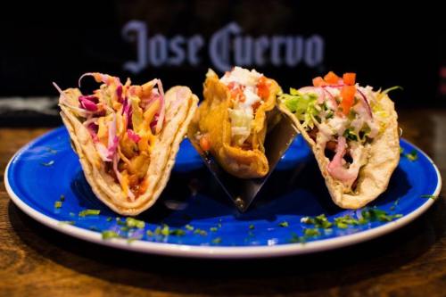 Three colorful tacos on a blue plate, filled with various toppings like lettuce, tomatoes, and pickled onions.