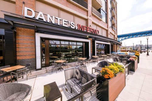 Exterior view of Dante's Inferno restaurant with outdoor seating and flowers, set against a city backdrop.