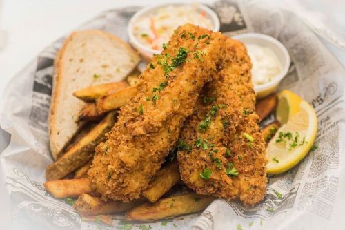 A plate of crispy fried fish fillets with fries, coleslaw, tartar sauce, and a slice of bread, garnished with parsley.