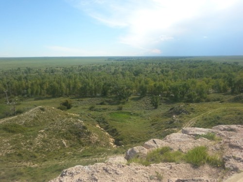 A panoramic view of a lush green landscape with rolling hills and a river, under a clear blue sky.