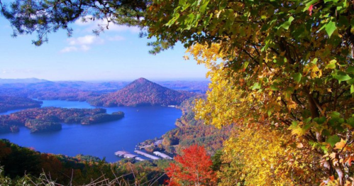 A scenic view of a lake surrounded by colorful autumn foliage and rolling hills under a clear blue sky.
