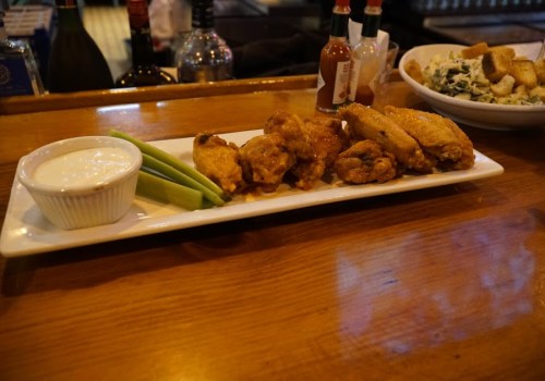 A platter of chicken wings with celery sticks and ranch dressing, served on a wooden bar top.
