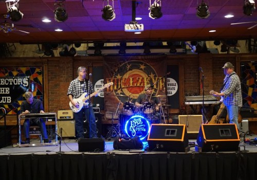 A band performs on stage with instruments, including a guitar and drums, in a lively club setting.