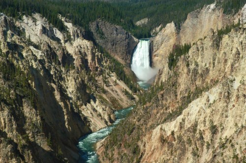 A stunning waterfall cascades down rocky cliffs, surrounded by lush green forests and a winding river below.
