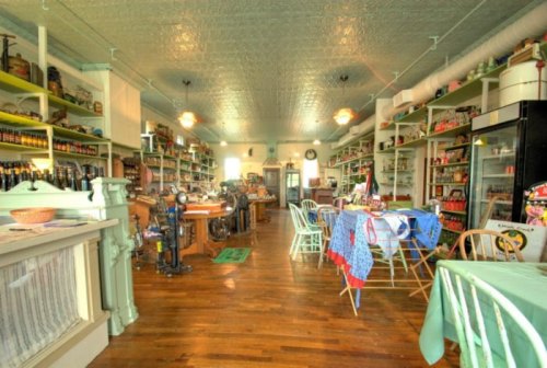 A vintage store interior with wooden floors, shelves filled with jars, and tables set for dining.