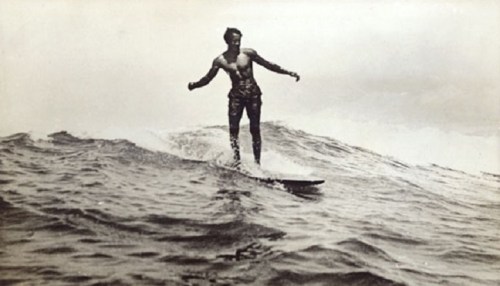 A vintage black-and-white photo of a man surfing on a wave, showcasing skill and balance on a surfboard.
