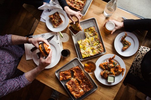 A table filled with various dishes, including pizza, shrimp, and drinks, as people enjoy a meal together.