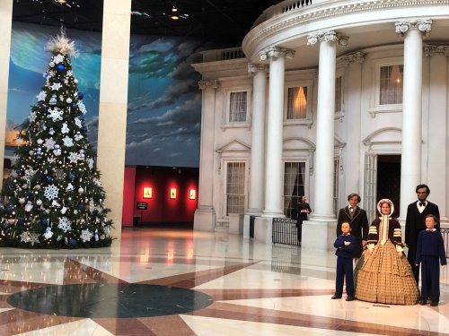 A holiday scene featuring a decorated Christmas tree and life-sized figures of historical characters in front of a building.
