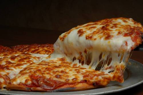 A close-up of a cheesy pizza with gooey melted cheese, fresh out of the oven, on a metal tray.