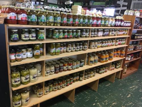 A wooden shelf filled with various jars of pickles, sauces, and preserves in a store.