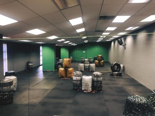 Indoor paintball arena with various obstacles made of tires and barrels, set against green and gray walls.