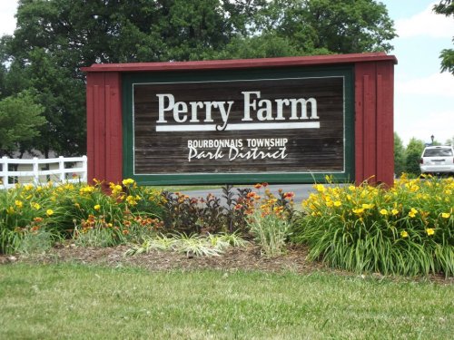 Sign for Perry Farm, Bourbannais Township Park District, surrounded by colorful flowers and greenery.