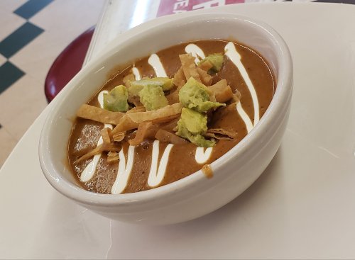 A bowl of creamy soup topped with avocado, tortilla strips, and a drizzle of sour cream.