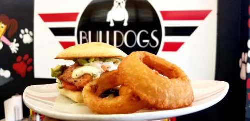A delicious sandwich with toppings and a side of crispy onion rings, set against a colorful Bulldogs restaurant backdrop.