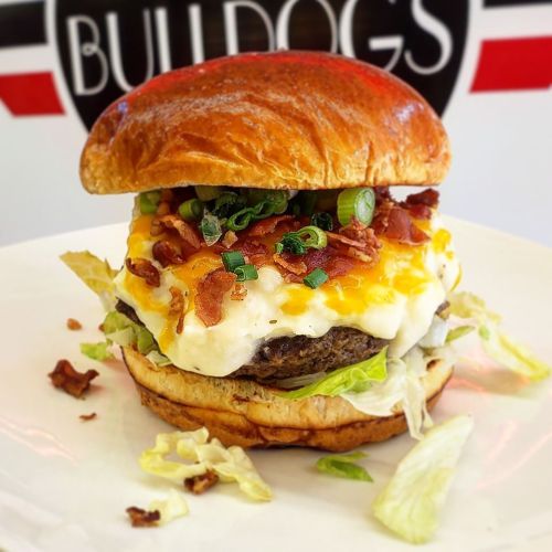 A delicious burger with a toasted bun, melted cheese, bacon, green onions, and lettuce on a white plate.