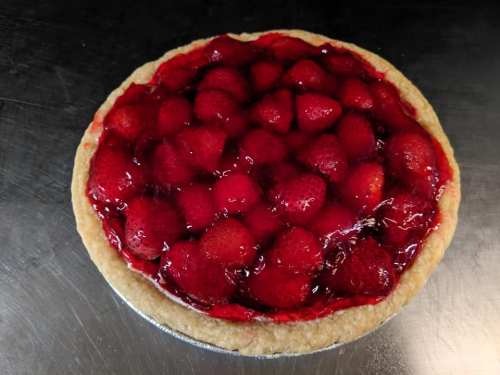 A round strawberry pie topped with glossy red glaze and fresh strawberries on a golden crust.