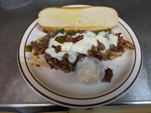A plate with a sandwich filled with beef, green peppers, and mayonnaise, alongside a side of dipping sauce.
