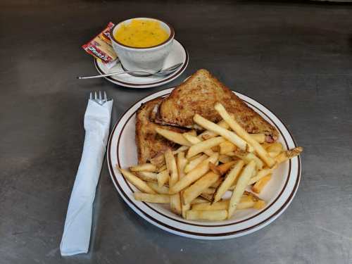 A plate with grilled cheese sandwiches, a side of fries, and a small bowl of soup on a metal surface.
