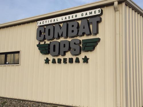 Sign for "Combat Ops Arena," a tactical laser games venue, displayed on a beige building exterior.