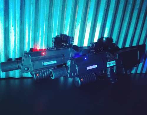 Two futuristic toy guns with blue and red lights, set against a textured metallic background.