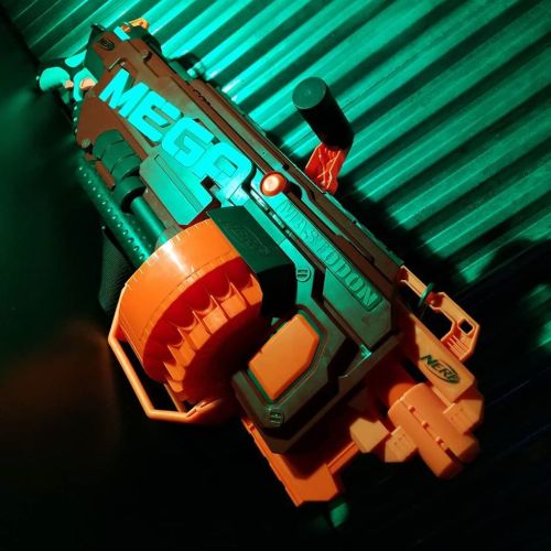 A brightly colored toy blaster with orange and gray details, resting on a textured surface illuminated by green light.