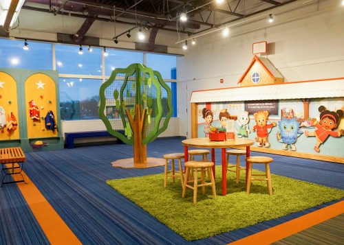 A colorful children's play area featuring a tree structure, a table with stools, and themed wall decorations.