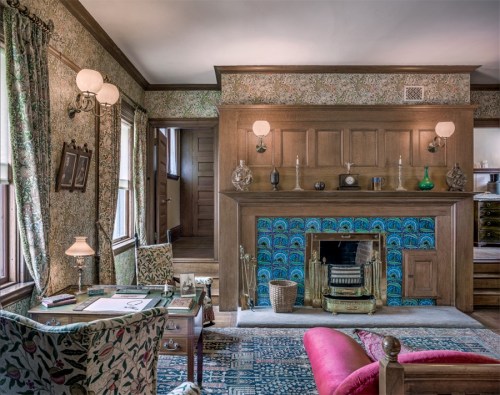 Cozy vintage living room with floral wallpaper, a fireplace adorned with blue tiles, and elegant furnishings.