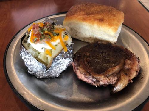 A plate with a baked potato topped with cheese and bacon, a biscuit, and a grilled meat patty.